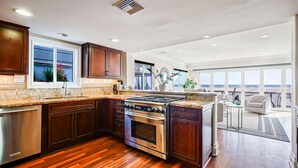 A modern kitchen with a large island, stainless steel appliances, and a view of the beach through large windows. - Entire Boardwalk Home on the Beach in Newport Beach with Beautiful Views (Newport Beach)