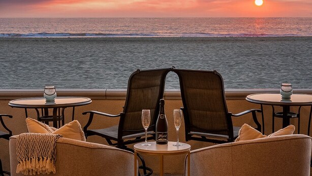 A sunset view from a balcony with two chairs and a table, a bottle of wine, and two glasses. - Entire Boardwalk Home on the Beach in Newport Beach with Beautiful Views (Newport Beach)