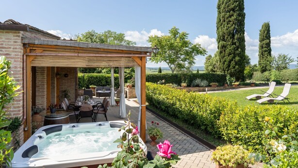 Ein Whirlpool in einer überdachten Außenbereich mit Tisch und Stühlen, umgeben von üppiger Bepflanzung und hohen Bäumen.