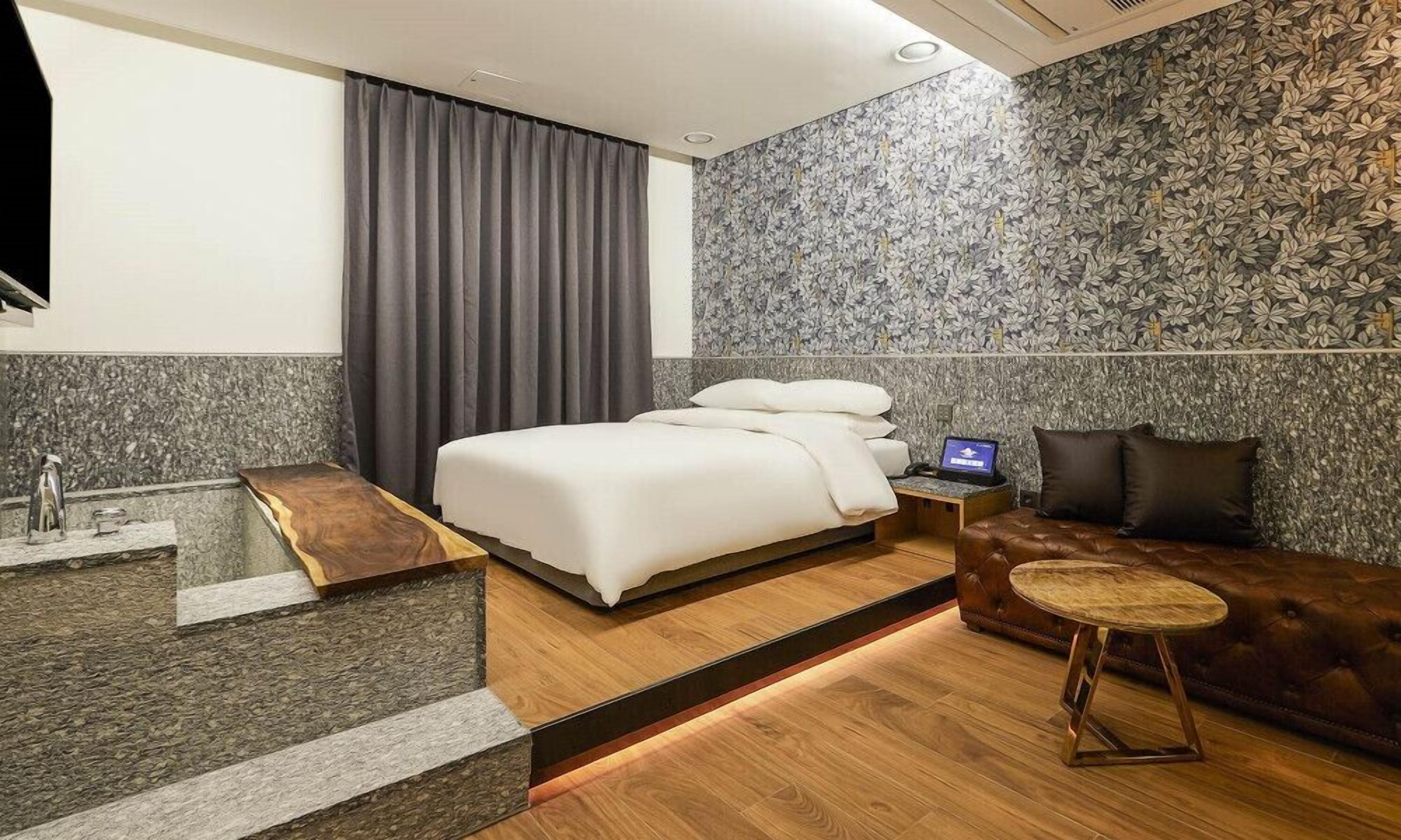 Una habitación de hotel moderna con una cama, un ordenador portátil sobre una mesita de noche, un sofá y una pequeña mesa redonda.