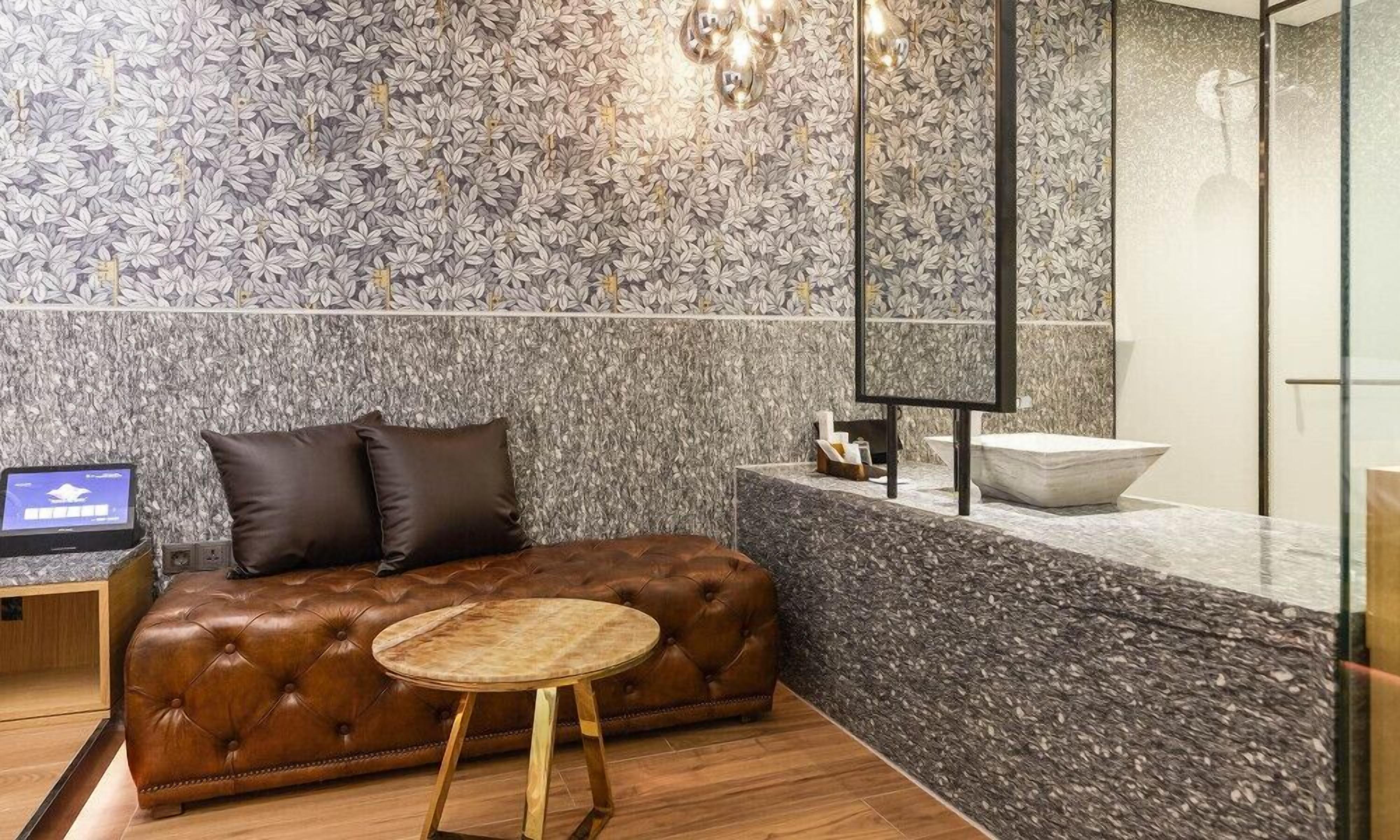 A modern lobby with a tufted leather sofa, a round wooden table, and a marble wall with a floral pattern.