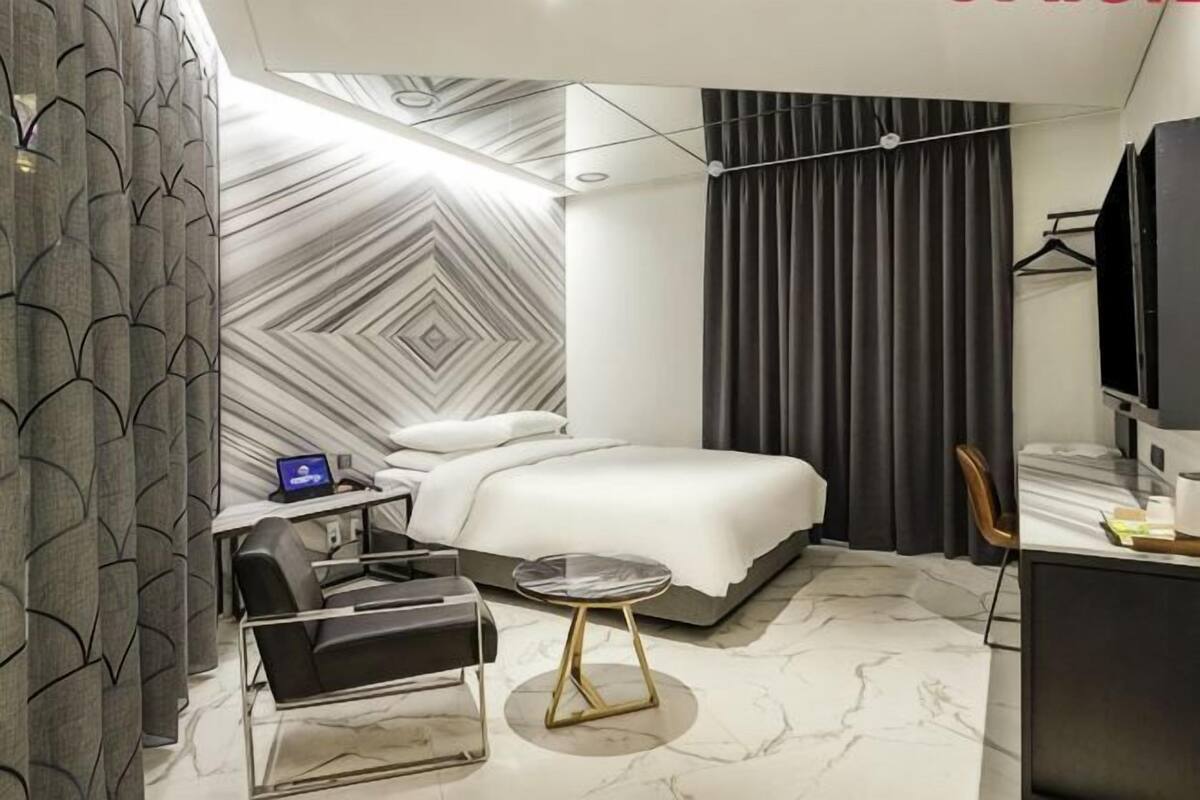 A modern hotel room with a bed, desk, chair, and a round table.