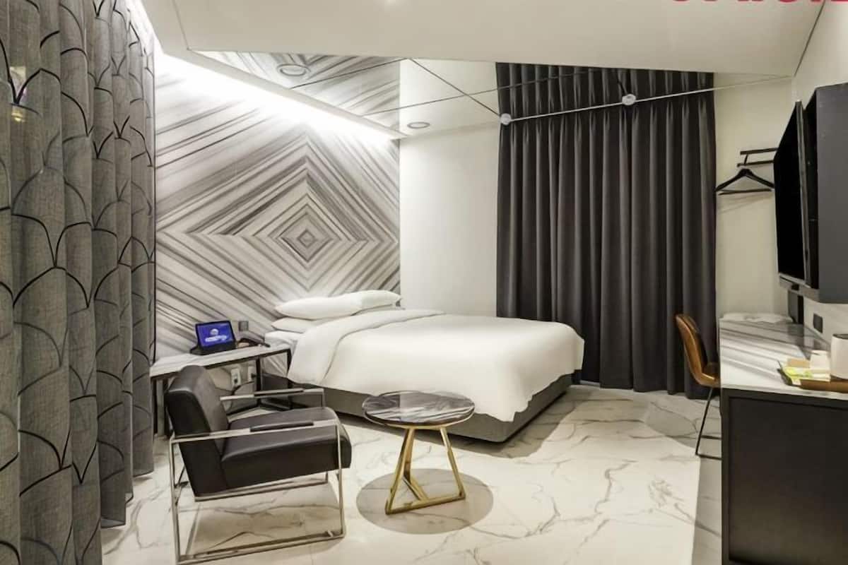Ett modernt hotellrum med en säng, ett skrivbord, en stol och ett runt bord.