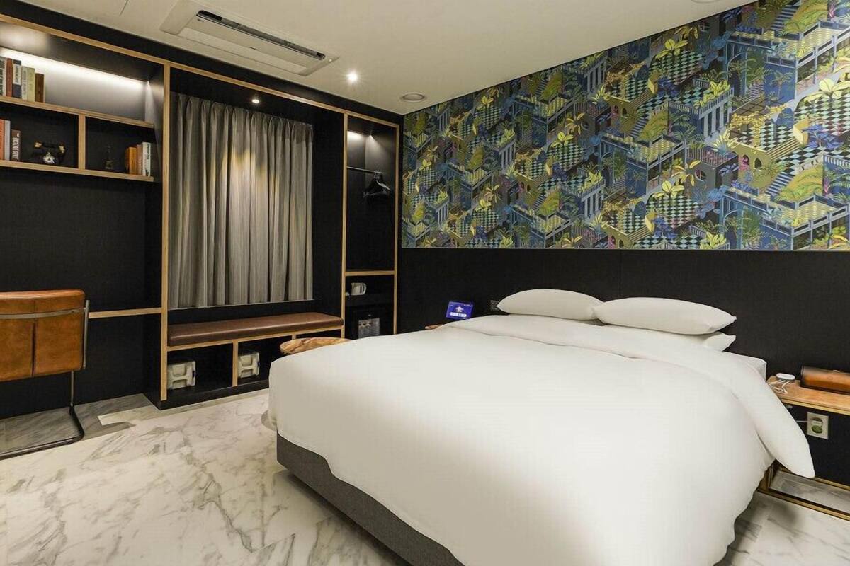 A modern hotel room with a large bed, a desk, and a bookshelf.