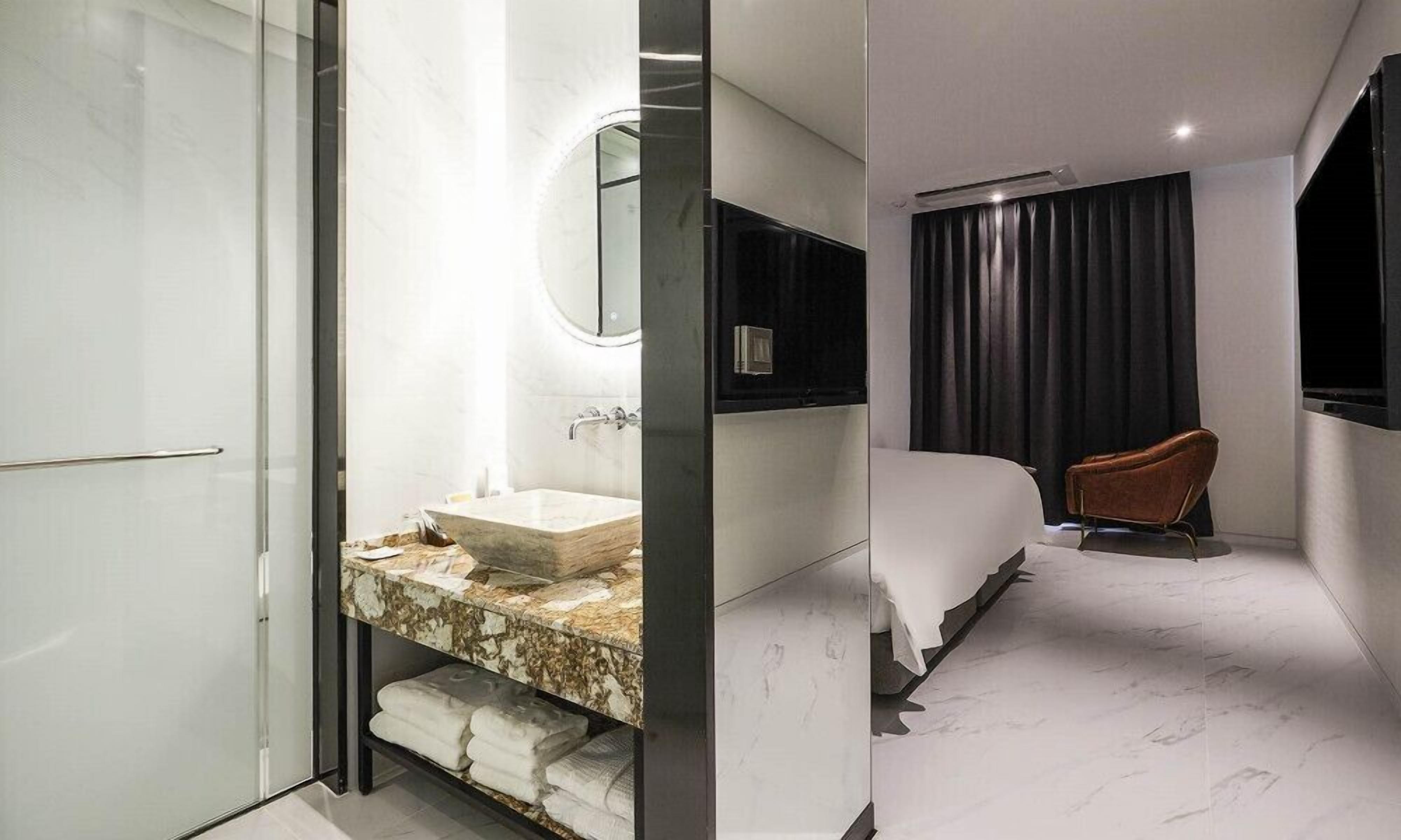 A modern hotel room with a marble bathroom, a large bed, a TV, and a separate seating area.