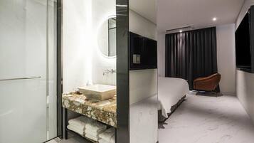 A modern hotel room with a marble bathroom, a large bed, a TV, and a separate seating area.
