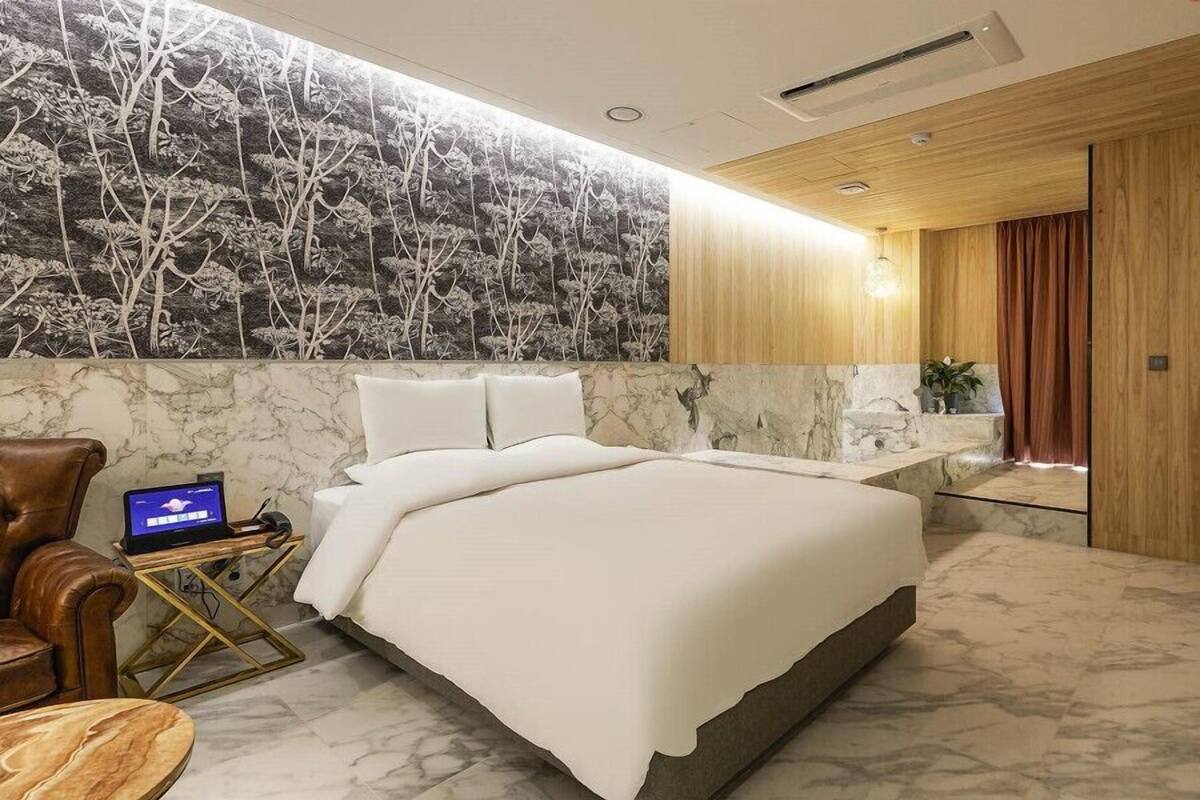 A modern bedroom with a large bed, a laptop on a side table, and a marble wall with a tree mural.