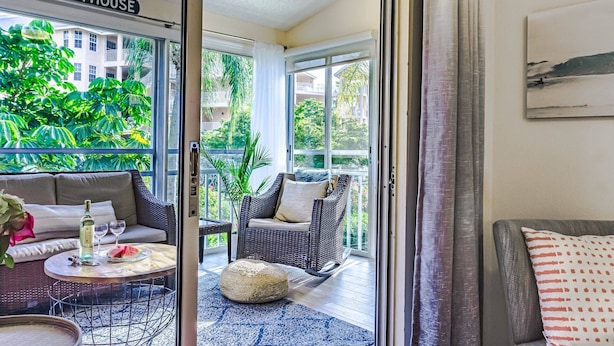 A room with a view of a balcony, wicker furniture, and a bottle of wine on a table. - Siesta Bayside 3BR Villa: Rare, Spacious Layout, Pickleball, Heated Pools, & Private Beach Access (Siesta Key)