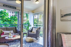 Una habitación con vista a un balcón, muebles de mimbre y una botella de vino sobre una mesa.
