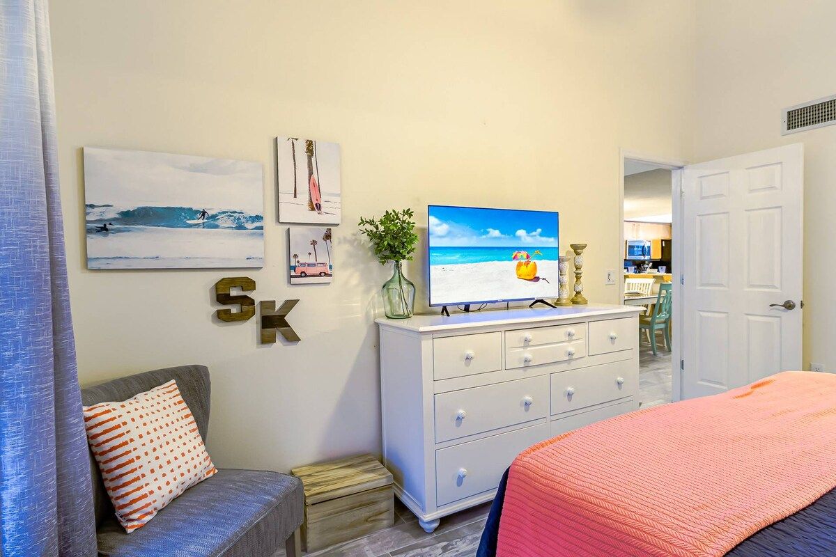Une chambre à coucher comprenant un lit, une commode, un téléviseur et des œuvres d’art murales.