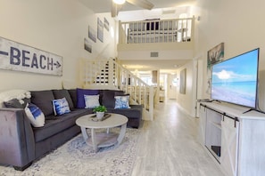 A spacious living area with a dark-colored sofa, a white coffee table, and a flat-screen TV on a wooden stand. - Spacious Siesta Bayside 3BR: Private Beach & Lanai (Siesta Key)
