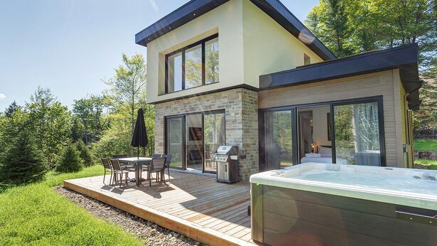 Uma casa moderna de dois andares com um pátio, área de estar externa e uma banheira de hidromassagem.