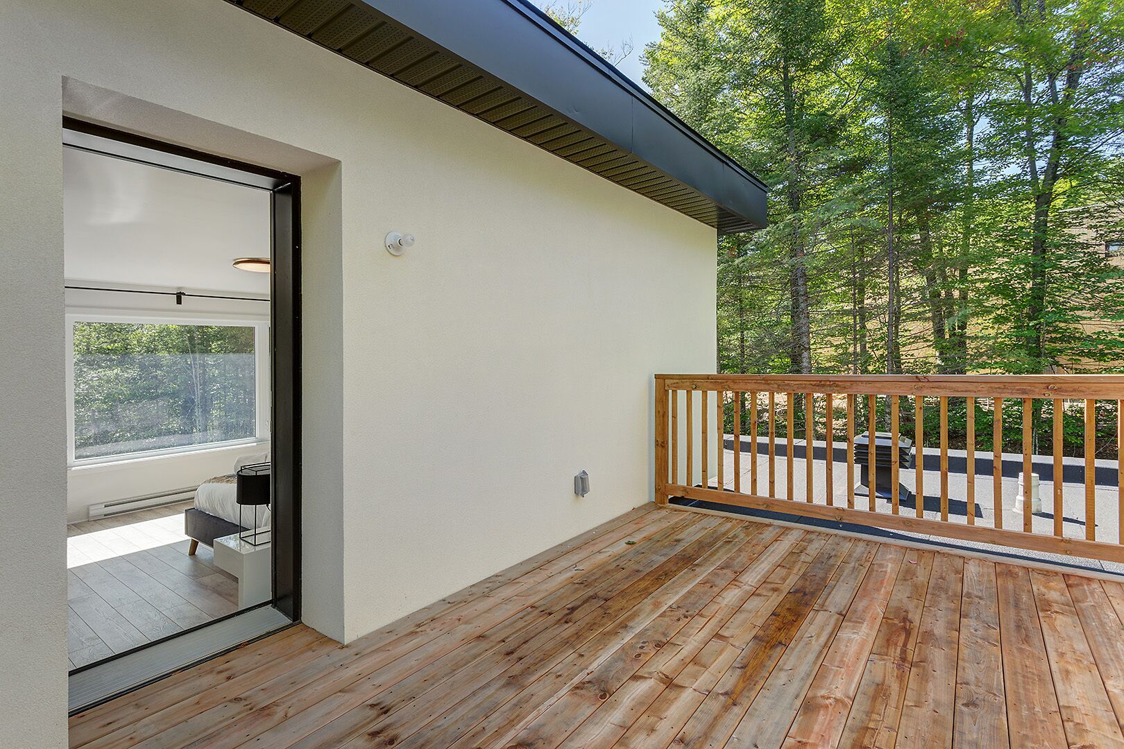 A modern room with a large window, a wooden deck, and a view of trees.