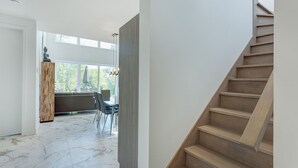 Um interior moderno com escada, área de refeições com luz natural e vista para o verde lá fora.