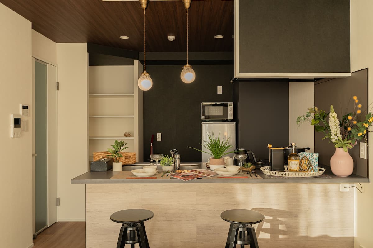 A modern kitchen with a central island, two stools, a microwave, and a refrigerator.