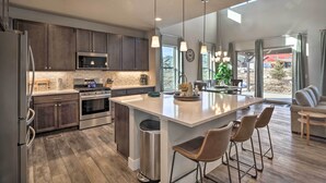 A modern kitchen with dark wood cabinets, stainless steel appliances, a large island with bar stools, and large windows offering a view of the outdoors. - Ski & Hike: Home w/ Hot Tub + Gas Grill in Granby (Granby)