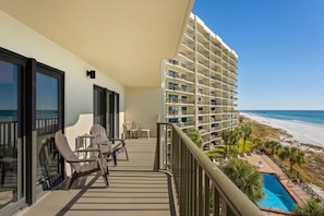 Ein Balkon mit Sitzgelegenheit im Freien, ein Pool und Blick auf Strand und Meer.