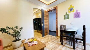 A modern hotel room with a wooden floor, a dining table with chairs, a potted plant, and a wall with motivational kitchen-themed decor.