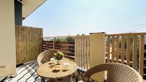 A balcony with wicker furniture, a table with two white mugs and a bowl of nuts, and a bamboo fence.
