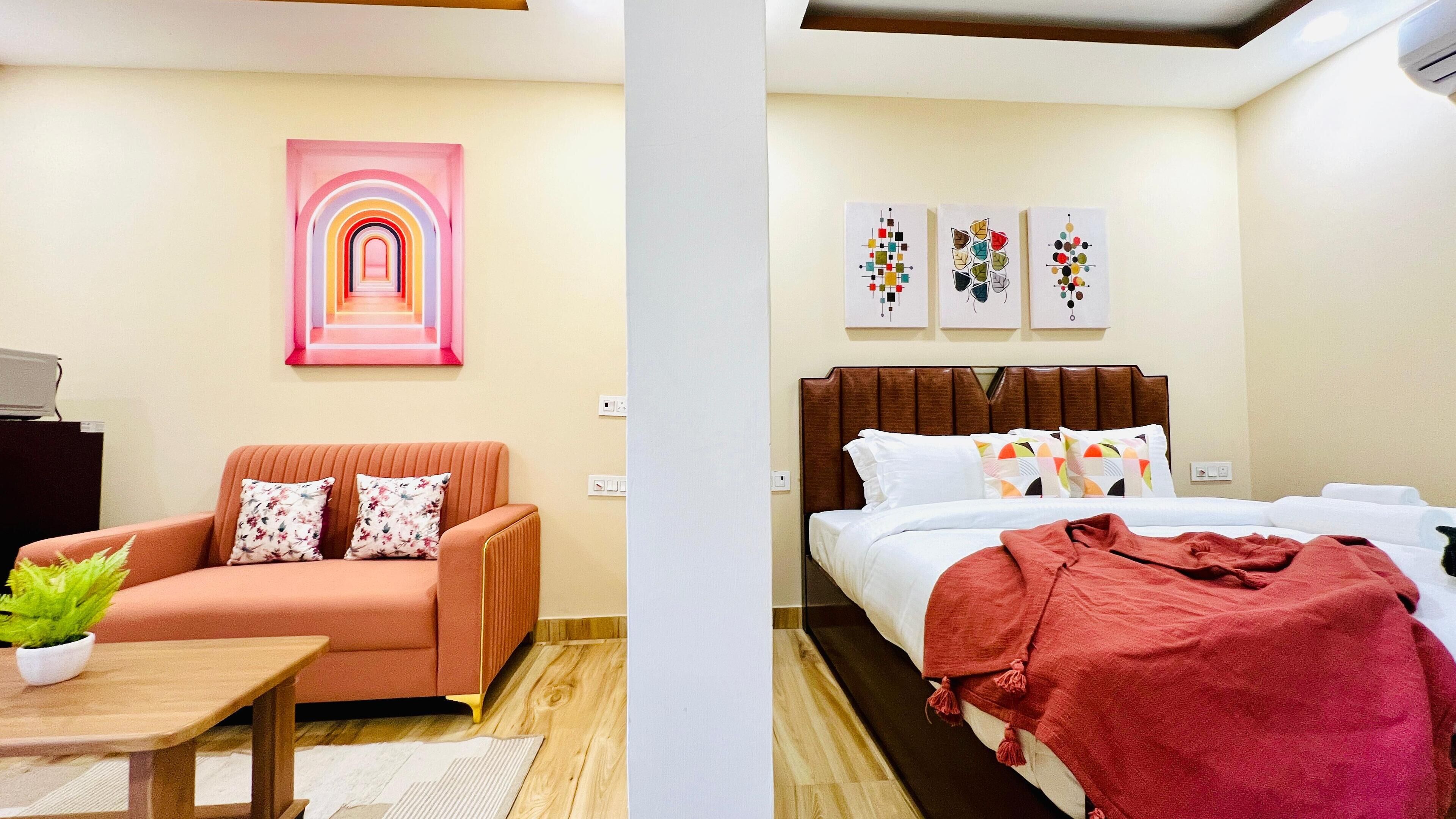 A hotel room with a sofa, a bed, a nightstand, and a wall with artwork.