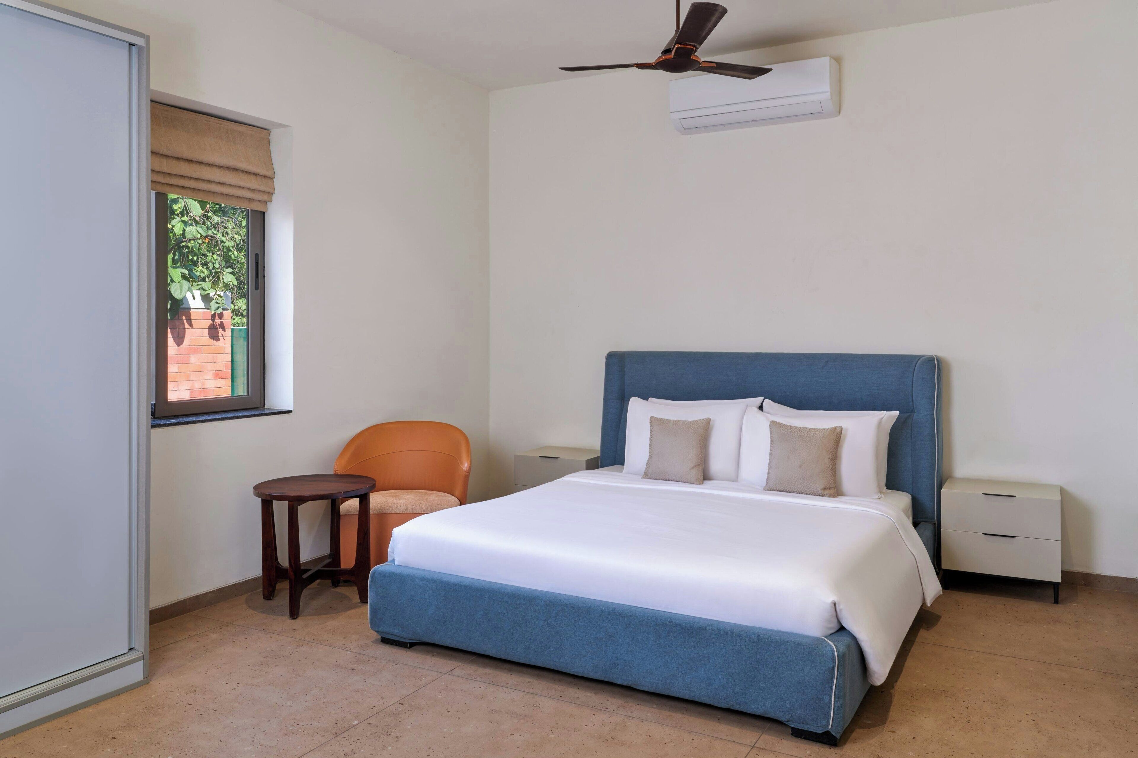 A bedroom with a bed, a chair, a small table, a nightstand, and a ceiling fan.