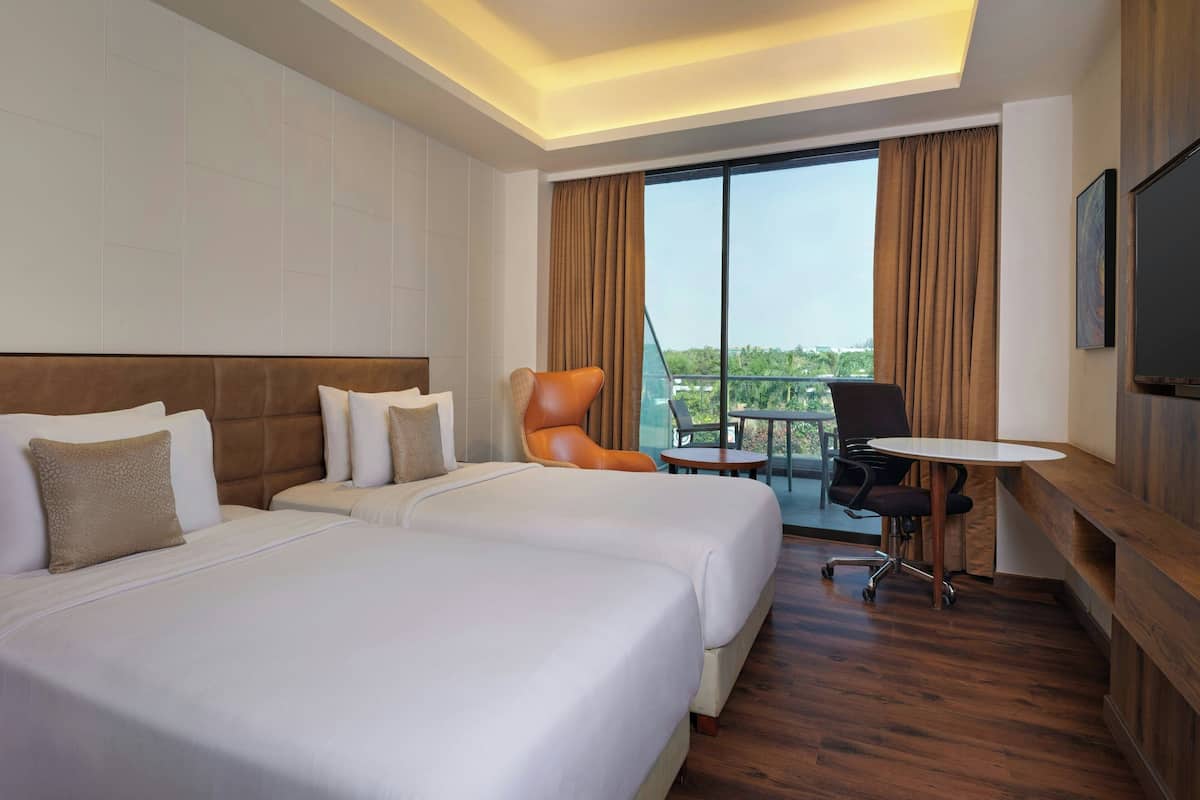 A hotel room with two beds, a desk, a chair, and a TV.