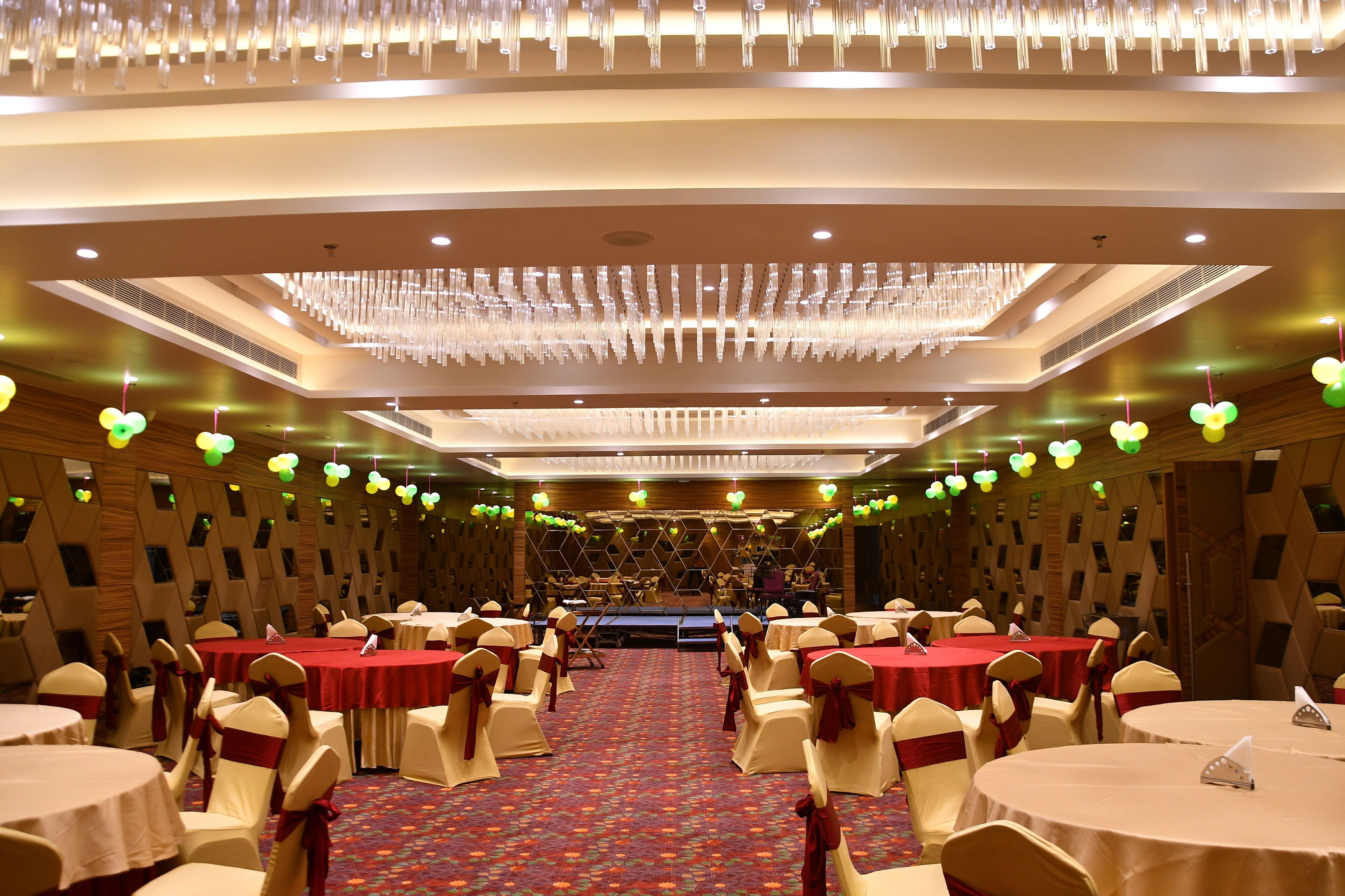 Un salón de banquetes con mesas redondas, sillas y un escenario.