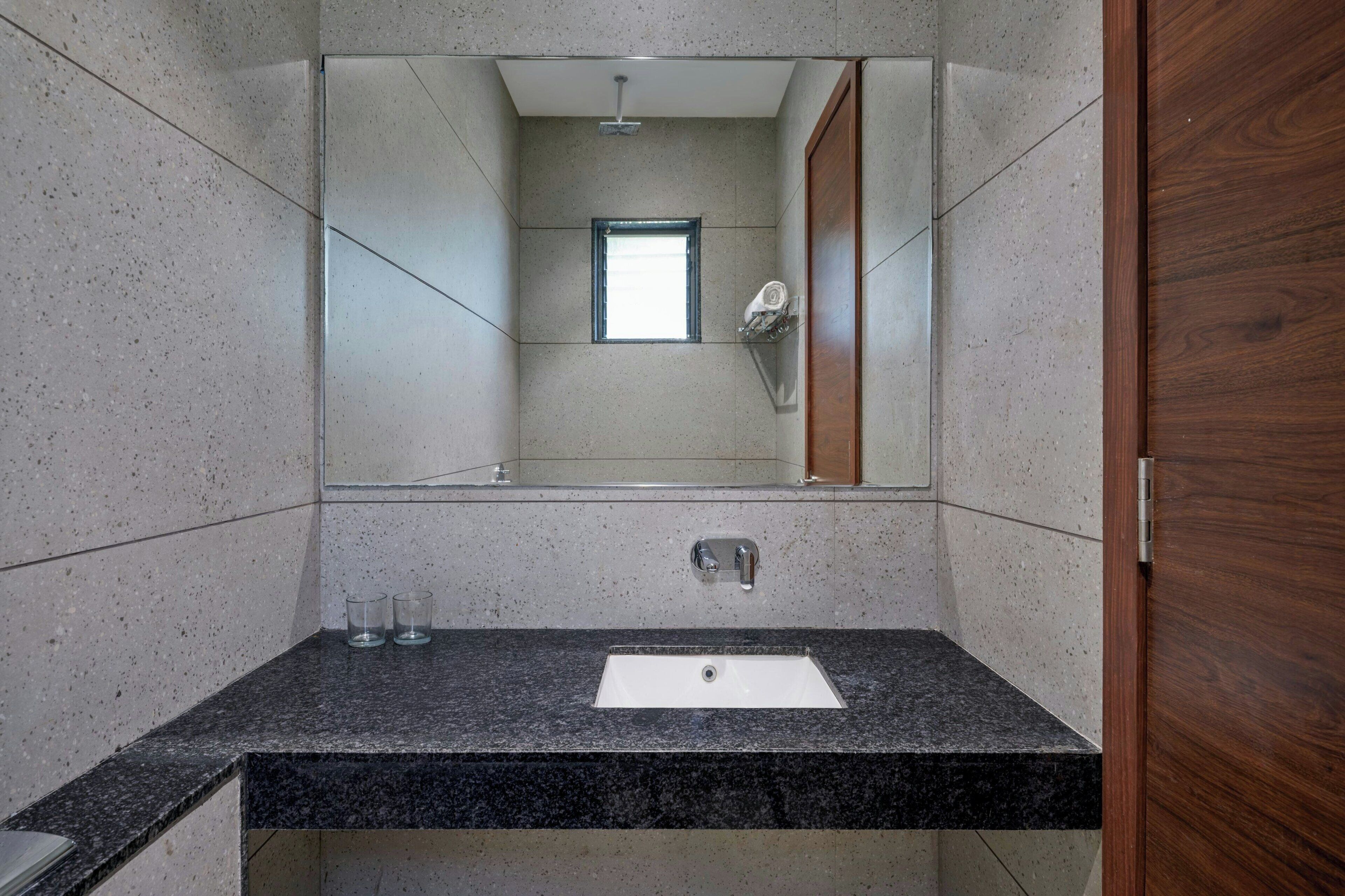 A bathroom with a granite countertop, a white sink, a mirror, and a wooden door.
