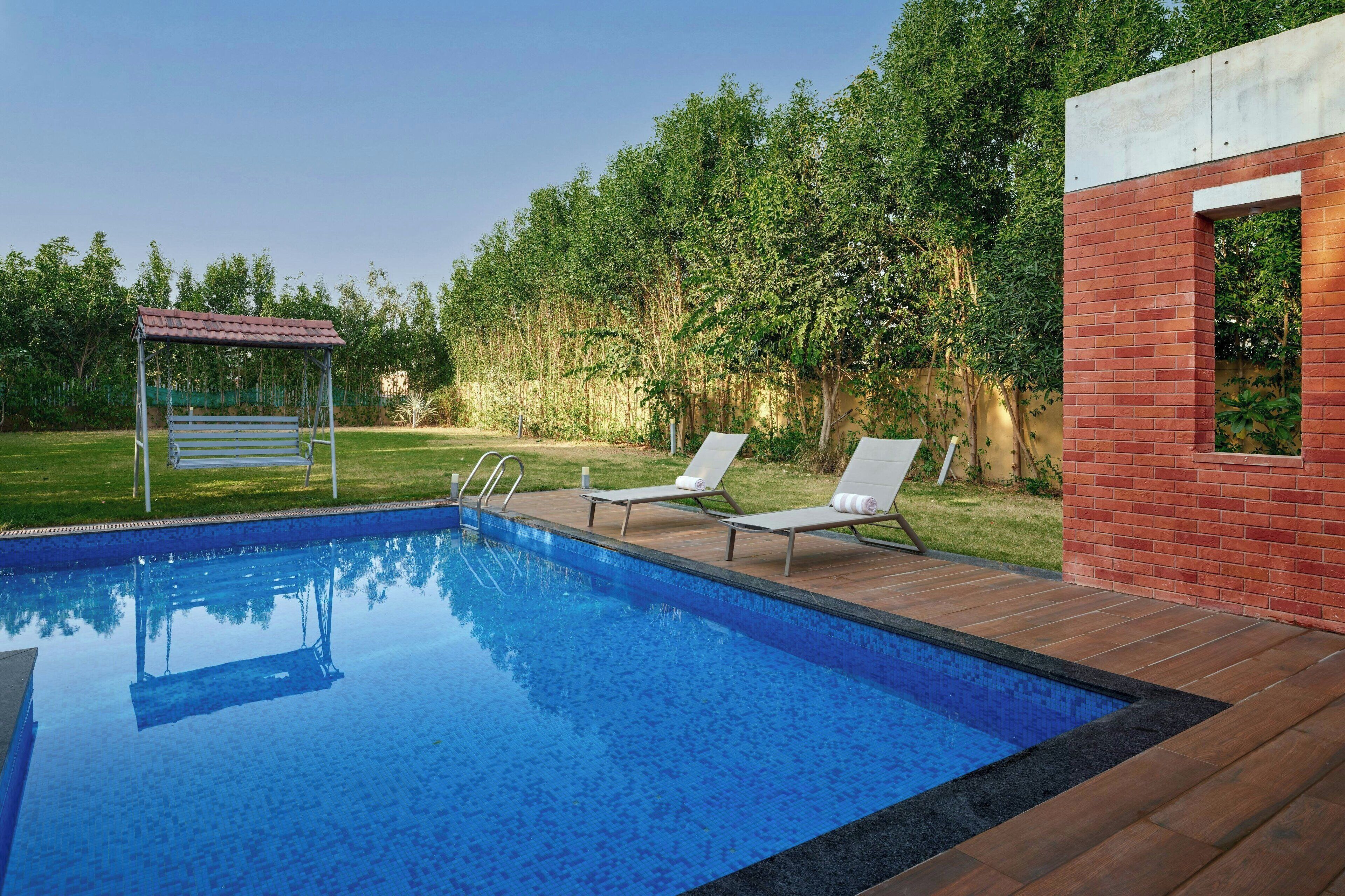 Una piscina con plataforma de madera, banco y sillas de descanso.