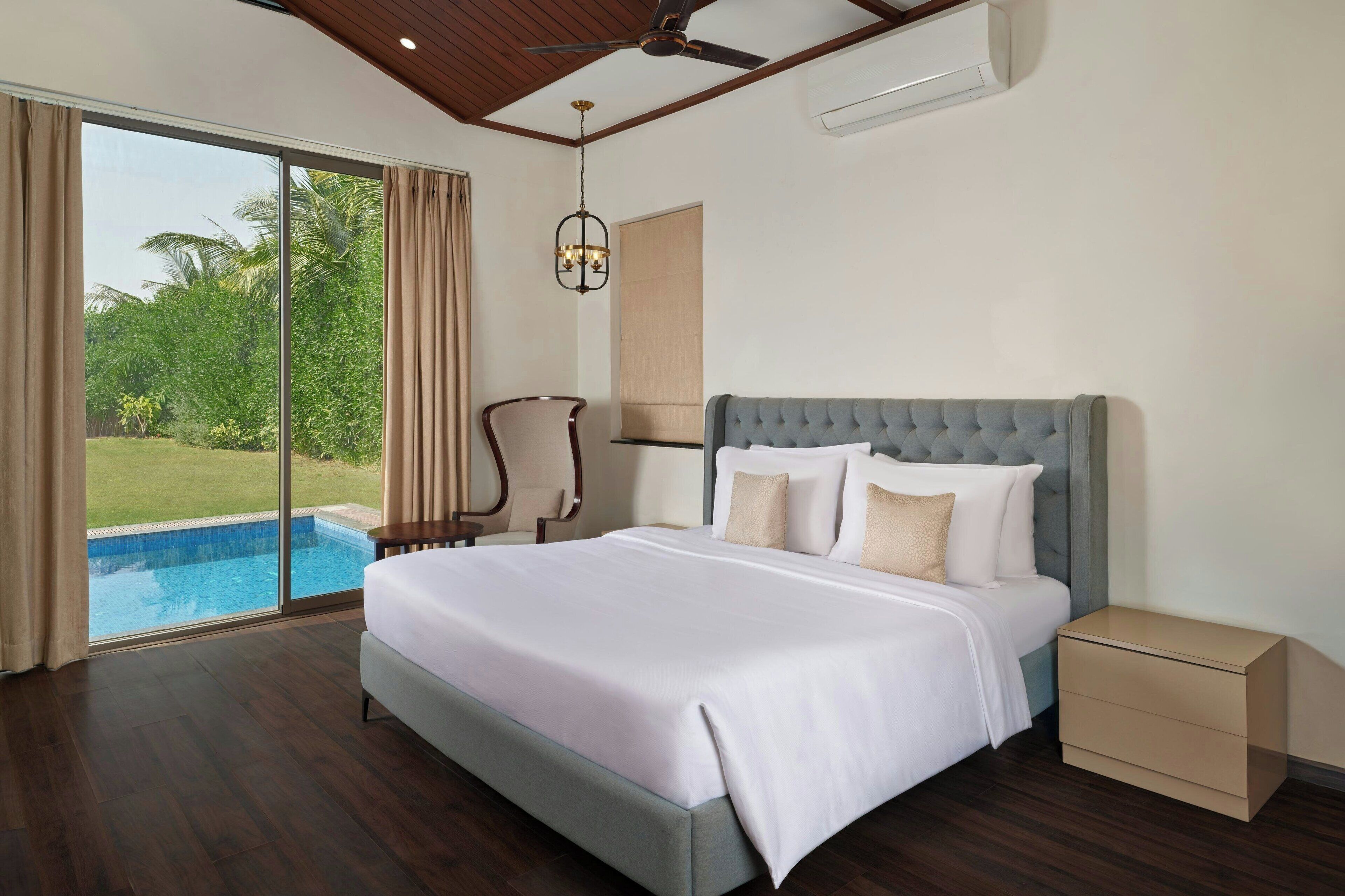A bedroom with a large bed, a nightstand, a chair, and a view of a swimming pool.