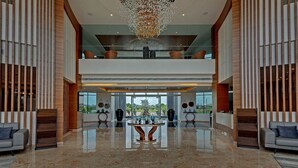 Un hall d’entrée spacieux avec un plafond haut, un lustre central et un balcon au deuxième étage agrémenté de sièges.