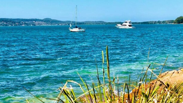 A calm sea with boats, clear water, and a rocky shoreline. - Large 6 bed home, walk to water, restaurants, pub, club, coffee, use of kayaks. (Salamander Bay)