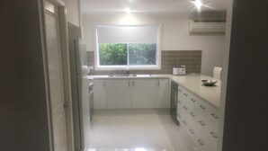 A modern kitchen with white cabinets, a stainless steel refrigerator, a dishwasher, and a window above the sink. - Large 6 bed home, walk to water, restaurants, pub, club, coffee, use of kayaks. (Salamander Bay)