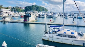 A marina with numerous boats docked, a small building, and a hill in the background. - Large 6 bed home, walk to water, restaurants, pub, club, coffee, use of kayaks. (Salamander Bay)