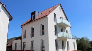 Un bâtiment à deux étages, avec un toit recouvert de tuiles rouges, des murs blancs et un balcon au deuxième étage.