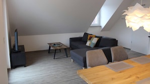 Un espace de vie moderne de style loft, doté d’un plafond en pente, d’un ensemble de canapés, d’une table à manger en bois et d’un luminaire au plafond original.