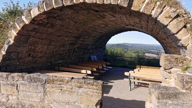 A stone archway with benches inside, overlooking a scenic landscape. - Ferienwohnung Altenstein (Maroldsweisach)