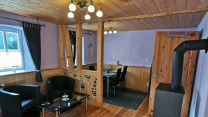 A cozy cabin interior with wooden floors, a dining area, and a wood stove. - Ferienwohnung Altenstein (Maroldsweisach)