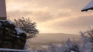 A snowy landscape with a stone wall, a metal fence, and a building with a sloped roof. - Ferienwohnung Altenstein (Maroldsweisach)