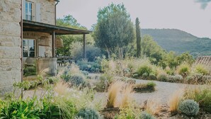 A stone building with a balcony, surrounded by a garden with various plants and a view of a hill. - Luxury estate with 60.000 sqm land near hilltop town Motovun (Motovun)