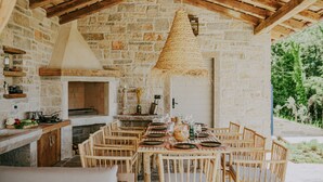 A rustic stone kitchen with a built-in oven, wooden dining table set for six, and a hanging woven light fixture. - Luxury estate with 60.000 sqm land near hilltop town Motovun (Motovun)