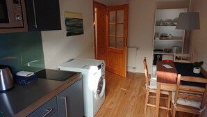 A compact kitchen with a washing machine, a stove, and a dining area with a table and chairs. - Gemütliche Ferienwohnung am Ortsrand (Kreuzwertheim)