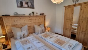 A double bed with a quilted headboard, a bedside table with a lamp, and a wooden wardrobe. - Cafe Altmühl, Ferienwohnungen Gästehaus Krimhilde direkt am Wasser (Essing)