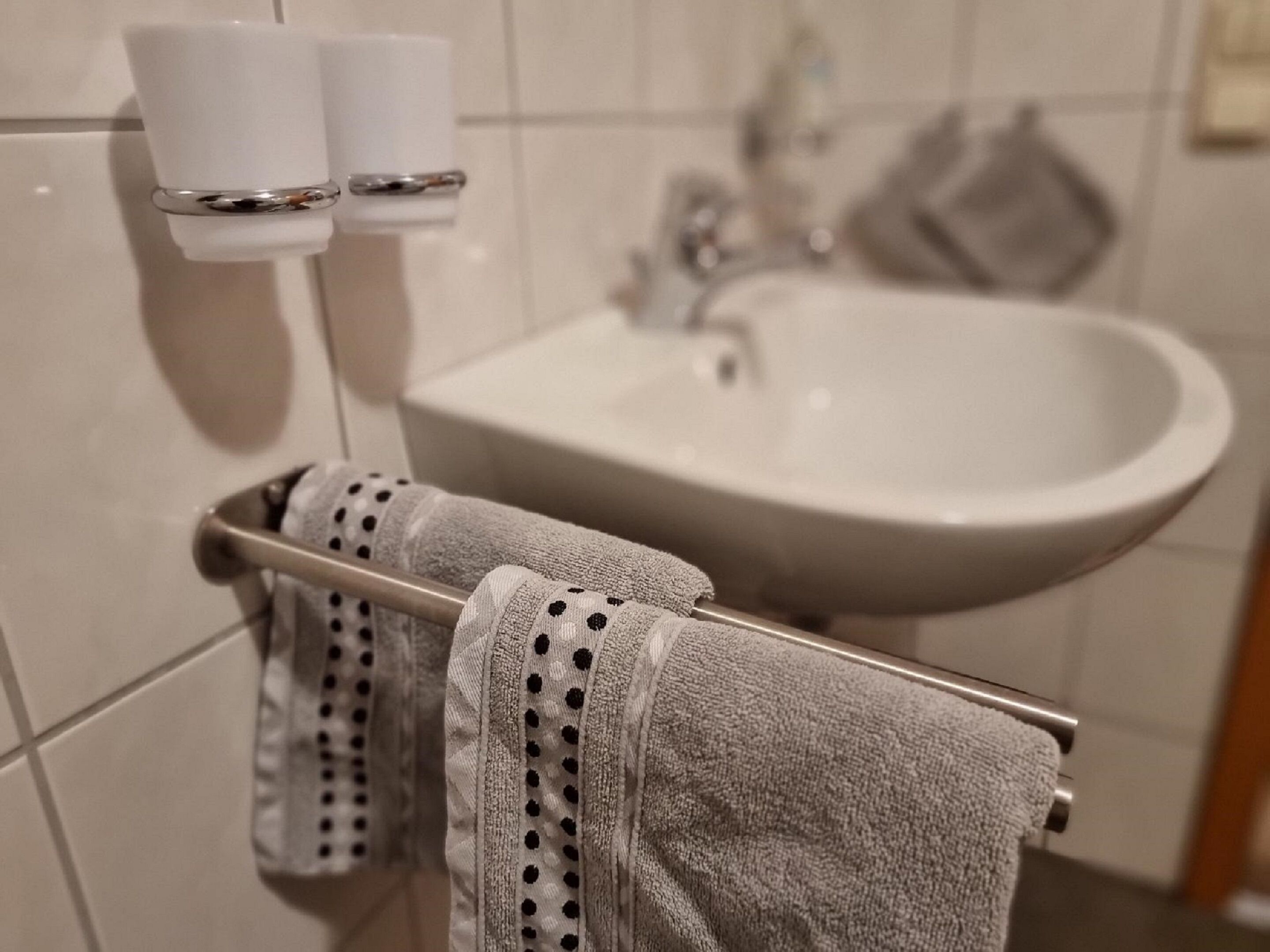 A bathroom with a sink, two white cups on a holder, and a towel rack with a towel.