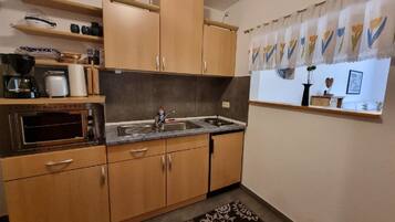 Una cucina compatta con mobili in legno, forno integrato, lavandino e finestra con tenda a fiori.