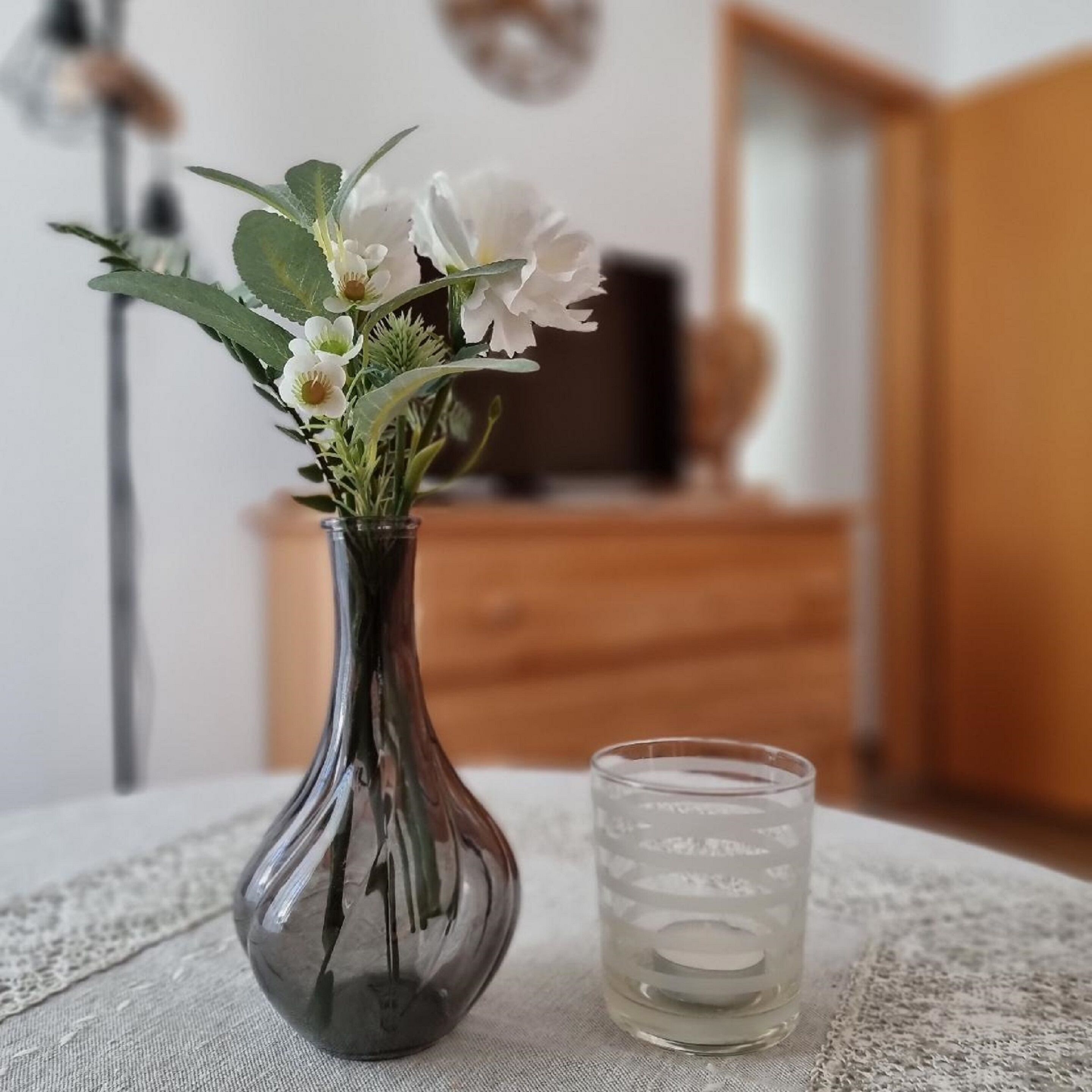 Um vaso com flores e um copo de água sobre uma mesa.