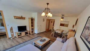 A cozy living room with a sofa, TV, wooden cabinet, and a dining area with chairs and a table. - Cafe Altmühl, Ferienwohnungen Gästehaus Krimhilde direkt am Wasser (Essing)