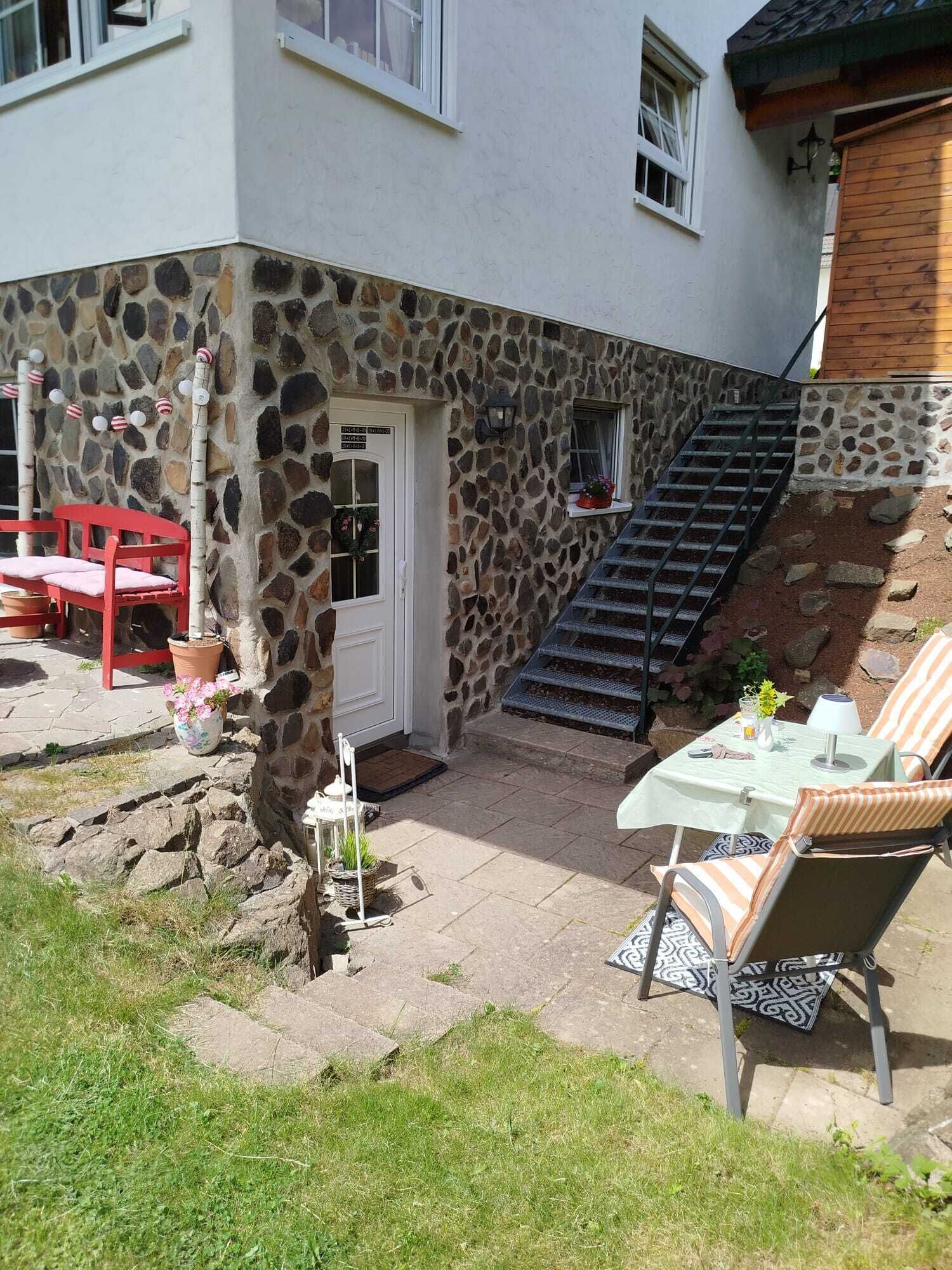 Ein Gebäude mit einer Steinfassade, einer weißen Tür, einer kleinen Treppe, Sitzgelegenheiten im Freien und einem Blumentopf.