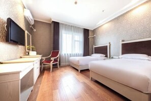 A hotel room with two beds, a desk, a chair, a TV, and a window with curtains.