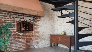 A room with a brick fireplace, a wooden cabinet, and a spiral staircase.